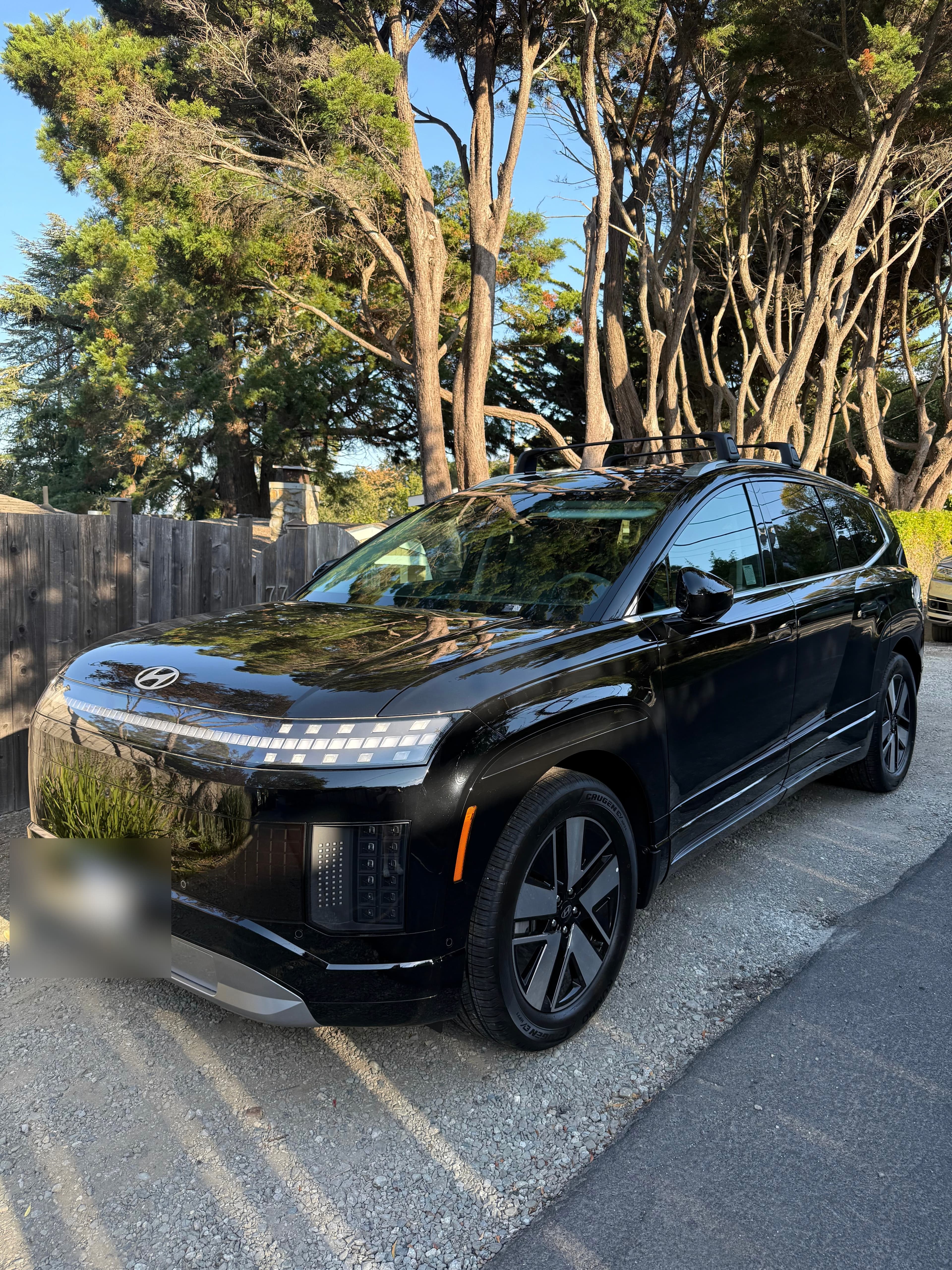 A black Hyundai IONIQ 9 on a gravel drive beneath Monterey cypress, delivered to a client in the Bay Area